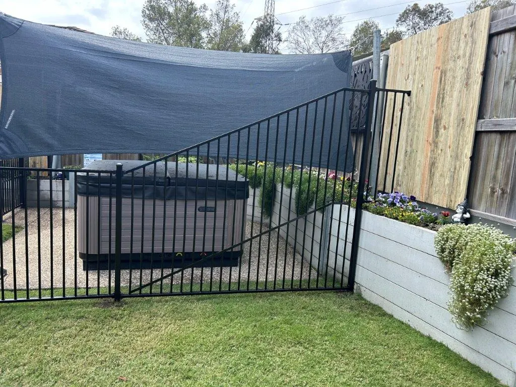 Black aluminium fence and raked gate enclosing a backyard spa