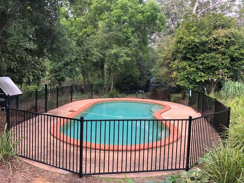 Black aluminium pool fence around a kidney-shaped pool in a leafy backyard