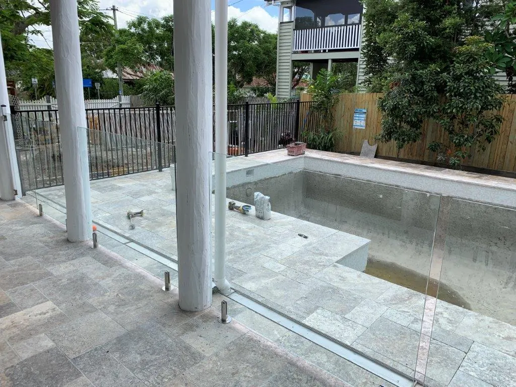 Frameless glass pool fence fixed in a floor channel and on spigots beside a verandah
