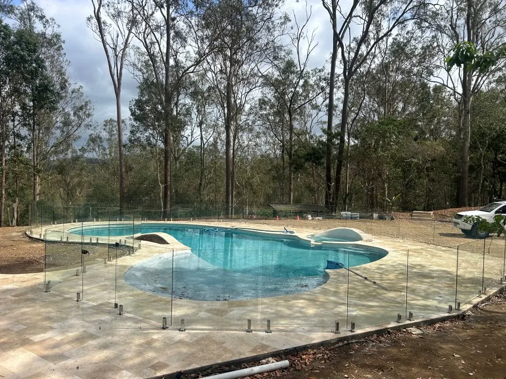 Frameless glass pool fence with polished spigots around a freeform pool on an acreage block