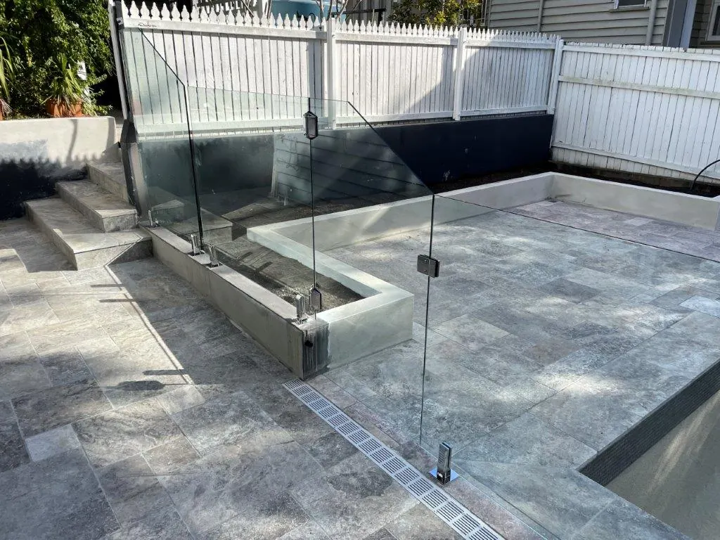 Frameless glass pool gate with stainless hinges beside paved steps