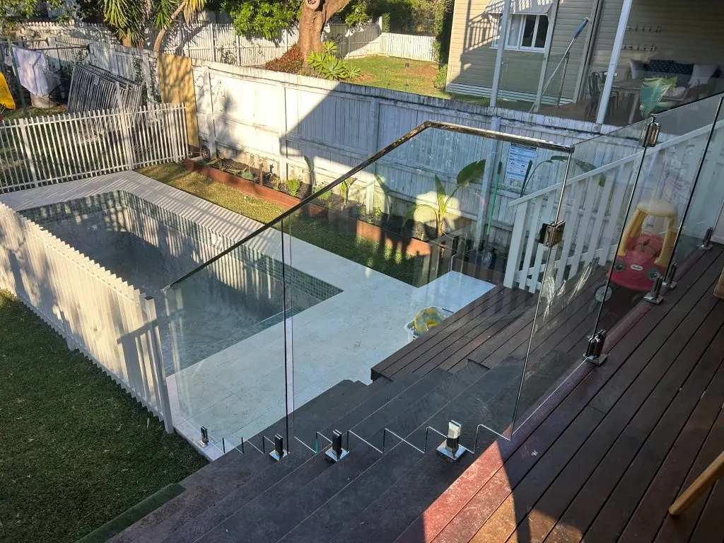 Frameless glass pool fence with a stainless top rail stepping down deck stairs