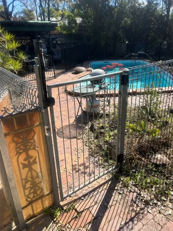 Pool gate with a new self-closing latch fitted to an older steel pool fence