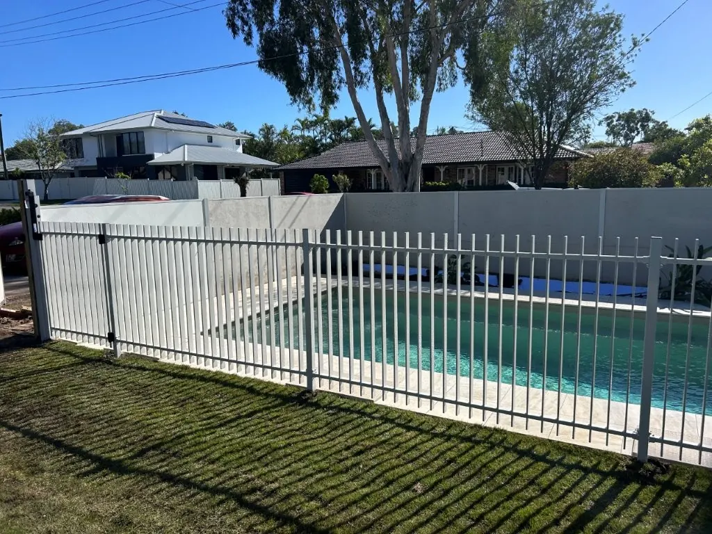 White aluminium pool fence with gate around a finished in-ground pool